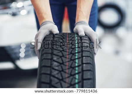 Closeup of mechanic hands pushing a black tire in the workshop. Royalty-Free Stock Photo #779811436