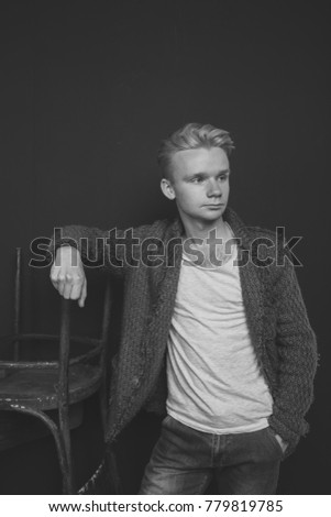 young stylish guy posing in Studio on a background of textured walls. emotional portrait: the mysterious looks and piercing image. man in winter clothes: warm sweater and t-shirt. black and white retr