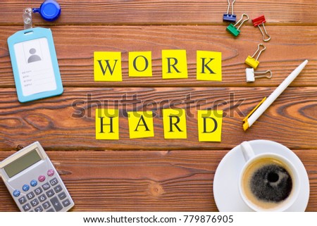 Work hard printed inscription in a frame of office items on a rustic wooden background, top view. Business and motivation concept. Space for your text or image.
