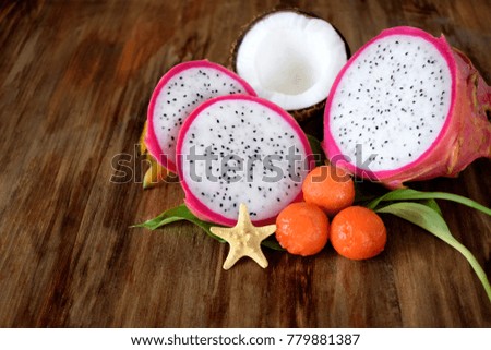 Pitahaya slices, papaya balls and a half of coconut on a wooden background. Tropic fruits
