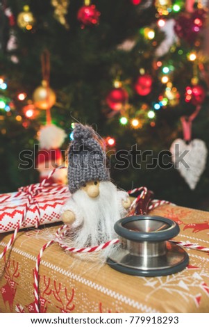 Close up view of a Santa figurine and a stethoscope on wrapped presents with blurred or bokeh christmas lights and tree in the background, medical christmas or holiday concept