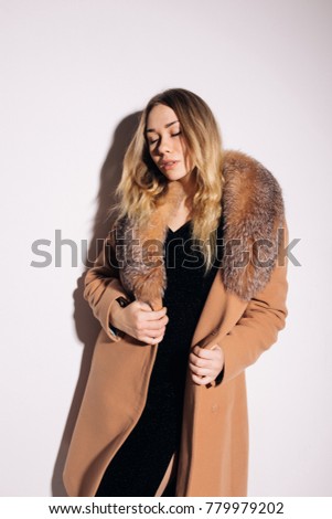 stylish young blonde girl posing in the Studio in the winter coat. emotional portrait. long healthy hair and pure skin. strict dress and warm shoes. natural makeup and expressive facial features