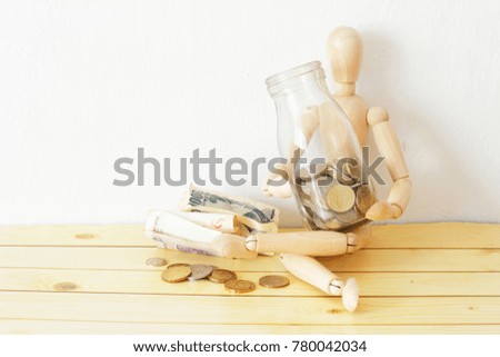 Concept of business and finance. Dummy / ball-jointed doll holding a glass jar full with coins