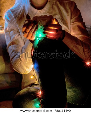 Female hands holding a cup of coffee, tea. Christmas and new year garland lights.