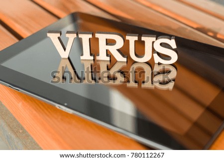 Word VIRUS with wooden vintage letters, tablet on a wooden bench background.