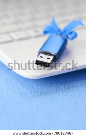 Brilliant blue usb flash memory card with a blue bow lies on a blanket of soft and furry light blue fleece fabric beside to a white laptop. Classic female gift design for a memory card