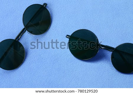 Two stylish black sunglasses with round glasses lies on a blanket made of soft and fluffy light blue fleece fabric. Fashionable background picture in female colors