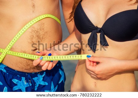 slender woman measures the volumes of a fat man on the beach