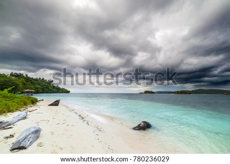 Incoming tropical stormy weather in the remote Togean Islands, Central Sulawesi, Indonesia. White sandy beach, blue lagoon, with scenic clouds, islets and fishermen village in the background.