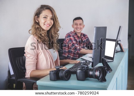 portrait of two photographers smiling while editing photos in their computer after photo session at office