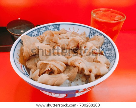 Pork over the rice in a bowl on orange table with a glass of water. Concept be used for Japanese restaurant business and present about Asia food. Blur picture.