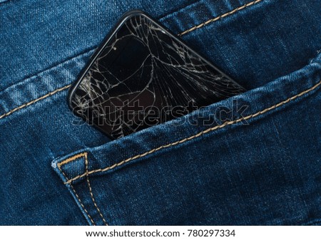 Mobile phone with a broken screen in the pocket of blue jeans.