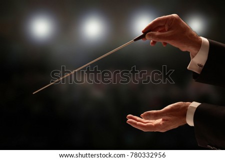 Conductor conducting an orchestra with audience in background Royalty-Free Stock Photo #780332956