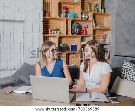 Smiling coworkers talking about successful common work while sitting with laptop computer in modern office space. Young two colleagues having conversation, waiting file download on portable net-book