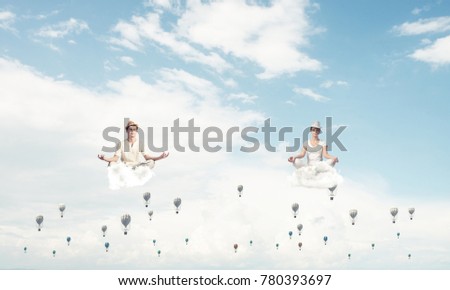Young couple keeping eyes closed and looking concentrated while meditating among flying aerostats in the air with cloudy skyscape on background.