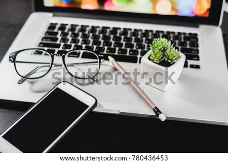 Modern office desk table with laptop computer, smartphone with bokeh screen over a notebook. Top view with copy space, flat lay.