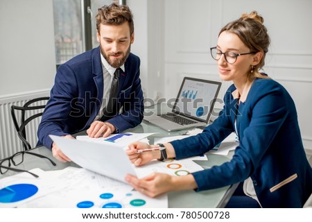 Marketer or analityc manager team dressed in suits working with paper charts and laptops at the white office interior Royalty-Free Stock Photo #780500728