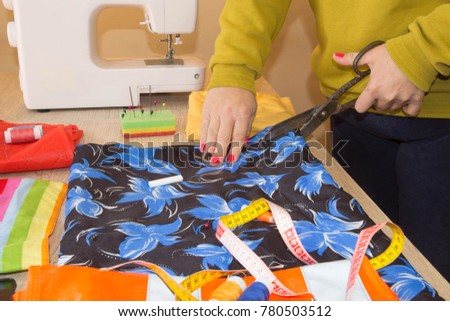 pattern, scissors, tape measure, and a sewing machine. Workplace of seamstress. Dressmaker cuts dress detail on the sketch lines. Garment industry, tailoring concept