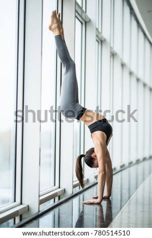 Young woman practicing yoga standing in handstand exercise, Pincha Mayurasana pose working out, against panoramic window