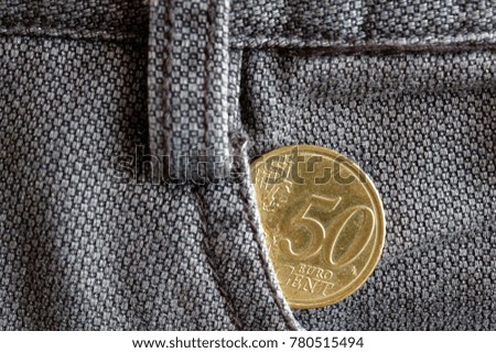 Euro coin with a denomination of fifty euro cents in the pocket of old brown denim jeans