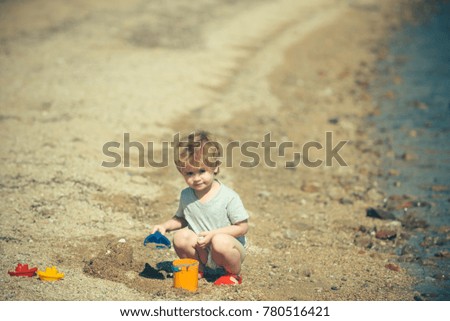 Boy playing on beach and looking at camera. Small beautiful cute child poses for advertising tourism, summer holidays and the sea side coast. Travel to the sea