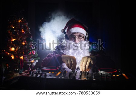 DJ Santa Claus mixing up some Christmas cheer. Dark disco club toned background. New Year's Eve event in the rays of light. Useful as poster or greeting card. Selective focus