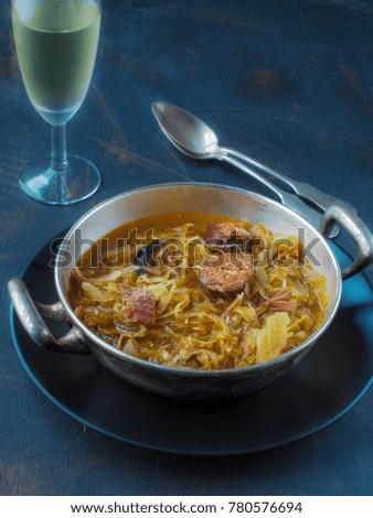 Cabbage soup in silver bowl and glass of white wine on dark background. Copy space.