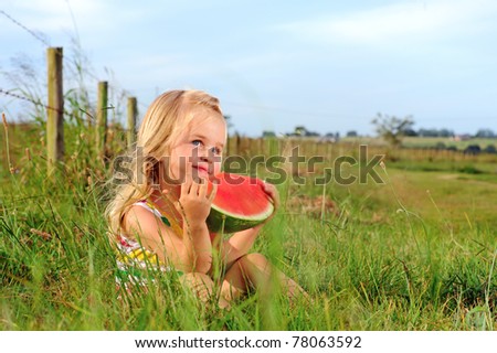 Cute blonde girl eats a watermelon in a field