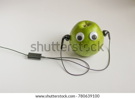 Green small apple with cute eyes and headphones on white background. Conceptual photo.
