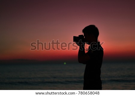 The silhouette of the photographer is being photographed by the beach during the light of day.