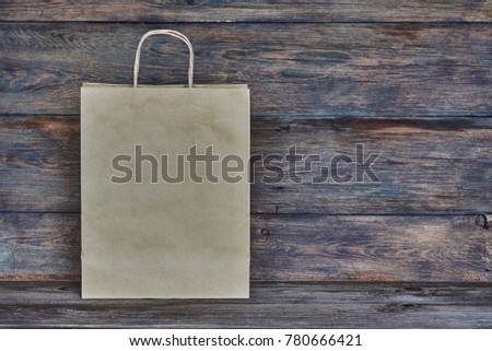 Mock-up of brown craft paper package with handles, empty shopping bag with area for your logo or design, wooden board in the background, food delivery, sale, consumerism and advertising concept.