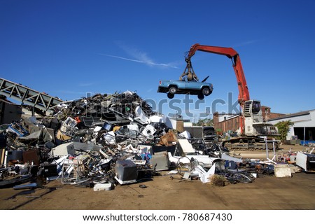 Crane with claw tossing trucks at scrapyard recycling center Royalty-Free Stock Photo #780687430
