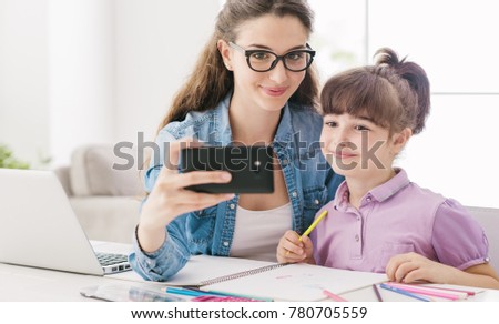 Cute girl and her young mother taking selfies with a smartphone at home, they are smiling and having fun