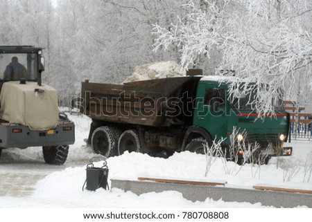 Excavator and lorry clean roads, streets from snow and ice. Winter industrial background