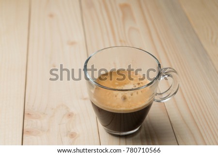 hot coffee with foam in a glass on a wooden table, a fragrant drink