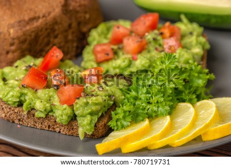 sandwiches from sauce guacamole with avocado, diced tomatoes, peppers and rye bread toast decorated sliced lemon, alligator pear fruit, parsley on plate, raw food