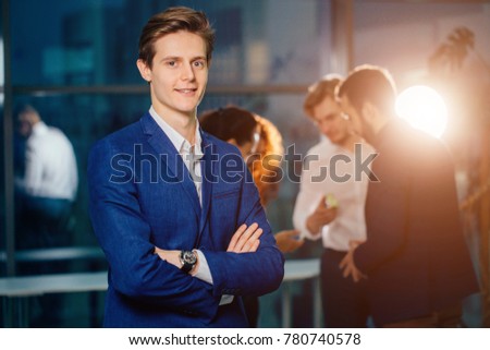 Successful small business owner standing with crossed arms with employee in background