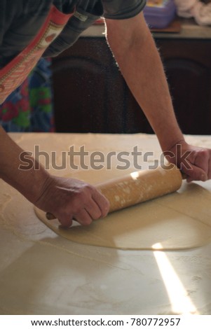 Hands roll the dough on the table with a rolling pin.
