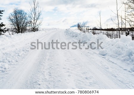 a rural snowy road with small snowdrifts on the roadside, on the edge of the road grow trees, winter nature on a sunny day
