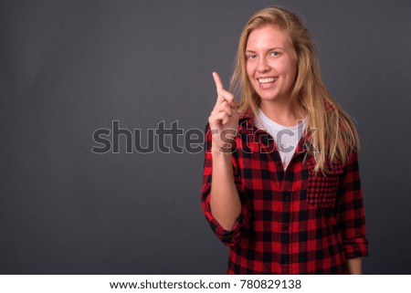 Studio shot of young beautiful woman with blond hair wearing red checkered shirt against gray background