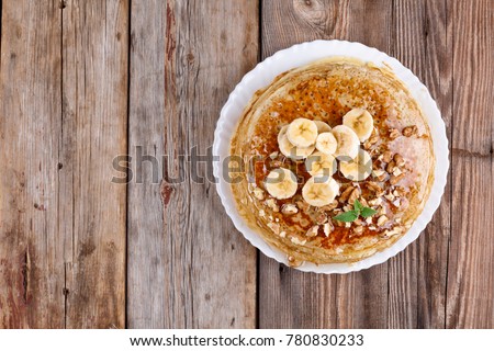 A pile of pancakes  with banana, walnuts and honey, and mint leaf, breakfast in rustic style, wooden background. Mardi Gras.
