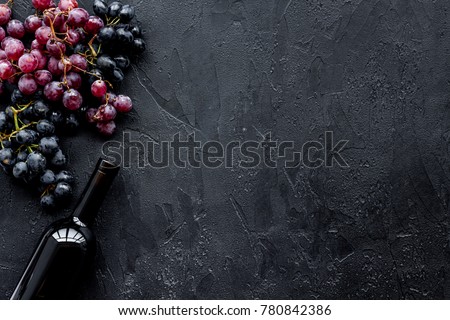 Wine bottle near bunches of red and black grapes on black background top view copyspace