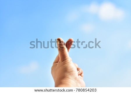 finger sign mini heart on blue sky and cloud. subject is blurred.