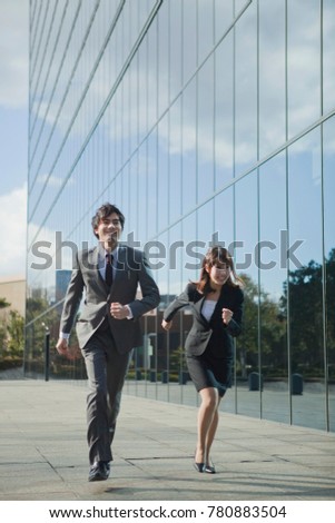 Japanese businessman and a business woman running in the front of the building