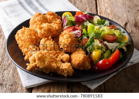 Fried chicken wings in breadcrumbs and fresh vegetable salad close-up on a plate. horizontal
