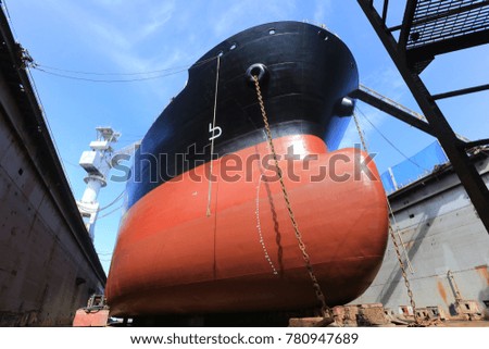 Tanker vessel on dock for repair black and red color lower down her anchor on dock floor. Background blue sky and green dock crane