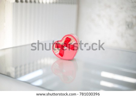 Heart-shaped box with red ribbon on reflective surface. 