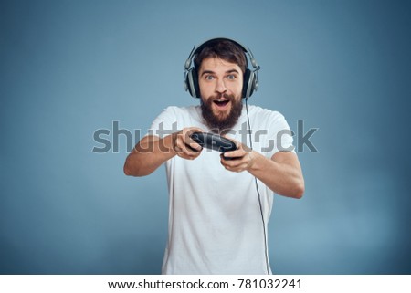  male joyful in headphones playing joystick in game console on blue background                              