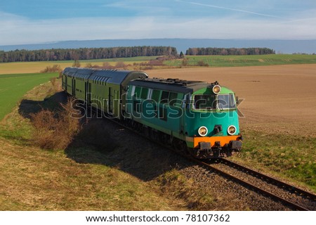 Passenger train hauled by the diesel locomotive passing the sunny landscape