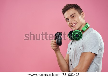  man smiling at the neck headphones in the hand joystick on the pink background, free place, technology                              